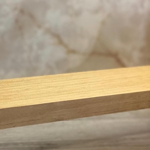 K&ouml;nnte beinhalten: Ein rechteckiges St&uuml;ck helles Holz mit einer sichtbaren Maserung. Das Holz hat eine glatte, flache Oberfl&auml;che und gerade Kanten, wobei die nat&uuml;rlichen hellbraunen und beigen Farbt&ouml;ne des Materials horizontal hervortreten.