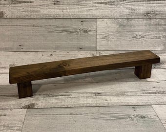 Könnte beinhalten: Ein rechteckiger Holzständer mit dunkelbraun gebeizter Oberfläche, bestehend aus einer langen, flachen Oberseite, die von zwei kurzen, dicken Blockfüßen an jedem Ende getragen wird und eine sichtbare Holzmaserung aufweist.