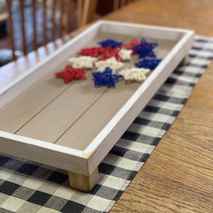 May include: A white wooden tray with four wooden legs and a gray wood top. The tray is decorated with red, white, and blue star-shaped ornaments.