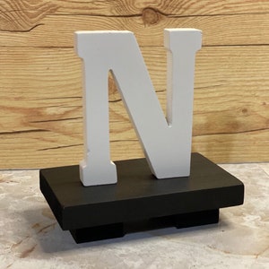 May include: White wooden letter N on a black wooden base. The base has a small lip around the edge and four small feet.