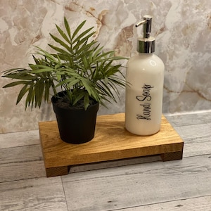 May include: A wooden tray with a small potted plant and a white ceramic soap dispenser with a silver pump. The dispenser has a black label that says "Hand Soap".