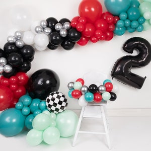 Pu&ograve; includere: Un palloncino nero con il numero due con una sedia bianca decorata con una ghirlanda di palloncini rossi, neri, bianchi, argentati, turchese e verde menta.