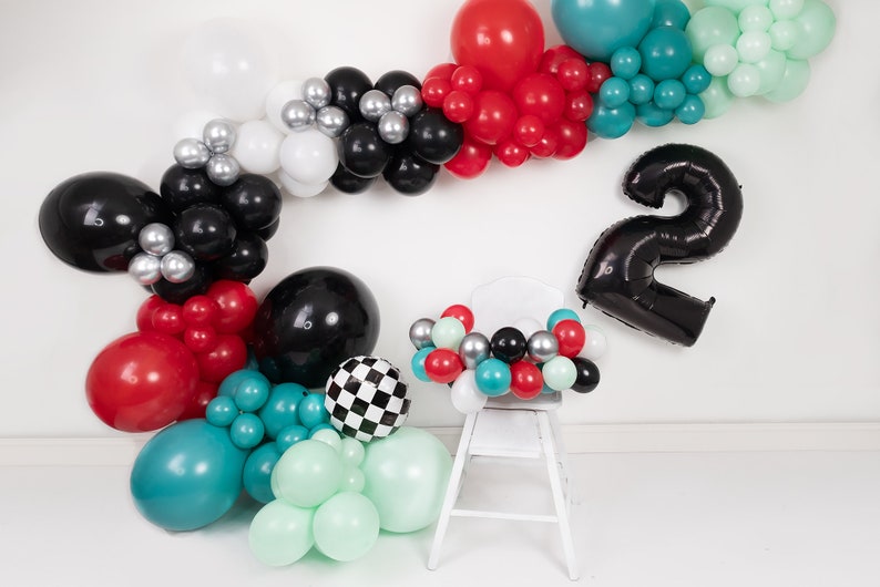 Pu&ograve; includere: Un palloncino nero con il numero due con una sedia bianca decorata con una ghirlanda di palloncini rossi, neri, bianchi, argentati, turchese e verde menta.
