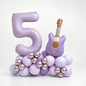 May include: A large lavender foil balloon shaped like the number 5 and a smaller lavender guitar-shaped foil balloon, both resting on a base of assorted light purple, lavender, and metallic rose gold latex balloons.