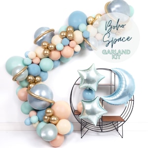 May include: A boho space themed garland kit with blue, gold, and cream balloons. The garland is made of balloons in the shape of planets, stars, and a crescent moon. The text "boho space garland kit" is written on a white circle.