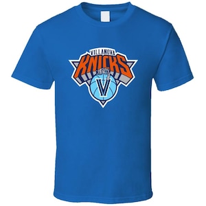 May include: A royal blue t-shirt with a white crew neck. The front of the shirt features a graphic of the New York Knicks logo with the word "Villanova" replacing "New York" in the logo.