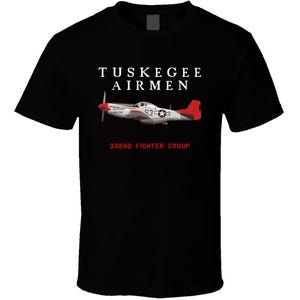 May include: Black t-shirt featuring the text "Tuskegee Airmen" above an illustration of a silver and red airplane. The text "332nd Fighter Group" is below the plane. The airplane has a white star on its side.