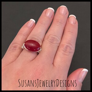 May include: A silver wire wrapped ring with a red oval gemstone.