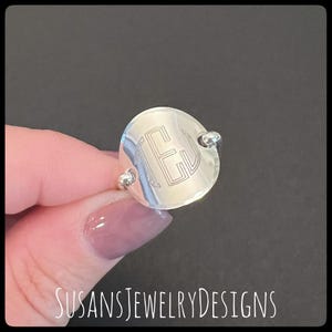 May include: A silver ring with a round, engraved monogram. The monogram is the letters "TE" in a simple, geometric font.