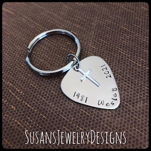 May include: Silver guitar pick keychain with a cross charm and the dates 1981 and 2021, and the name Wesley engraved on it.