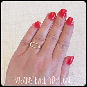 May include: A silver-colored ring with a rectangular link design. The ring is worn on a finger with red nail polish. The text "SUSANSJEWELRYDESIGNS" is visible at the bottom of the image.