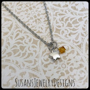 May include: A silver chain necklace with a silver star charm and a small amber crystal. SUSANSJEWELRYDESIGNS is printed at the bottom of the image.