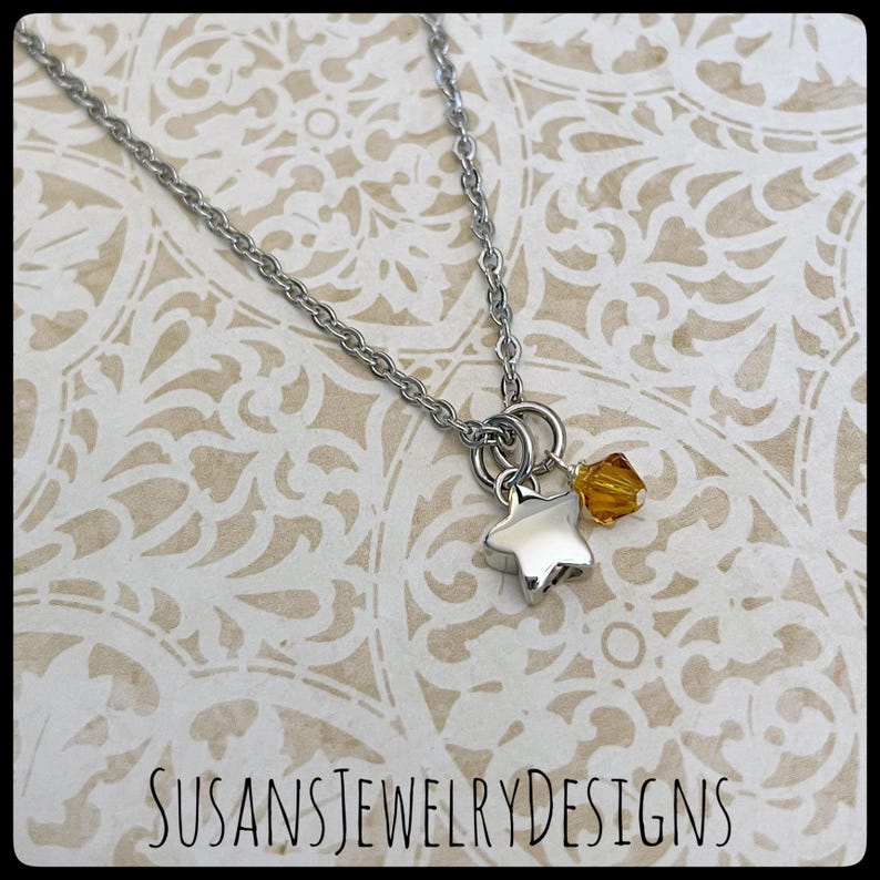 May include: A silver chain necklace with a silver star charm and a small amber crystal. SUSANSJEWELRYDESIGNS is printed at the bottom of the image.