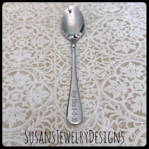 Puede incluir: Una cuchara plateada brillante con un mango largo. El mango est&aacute; grabado con el nombre "Bryn Ellen" y la fecha "8-11-20". La cuchara se muestra sobre una superficie crema estampada. El texto "SUSANSJEWELRYDESIGNS" est&aacute; en la parte inferior.