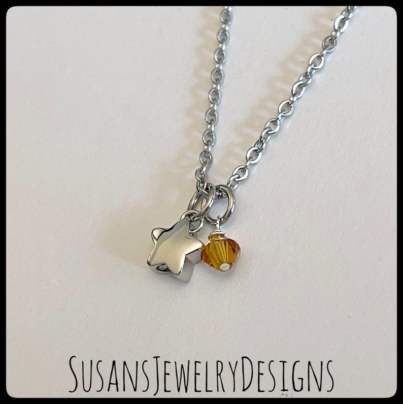 May include: A silver chain necklace with a silver star charm and a small amber-colored crystal bead.