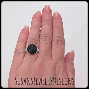 May include: A silver wire wrapped ring with a black lava rock stone. The ring is on a person's finger.