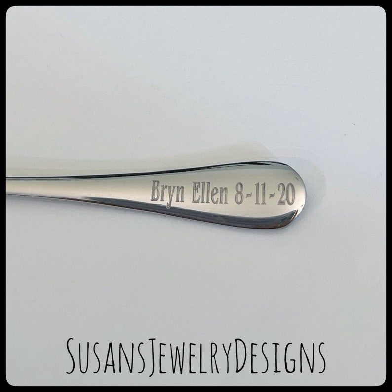 Puede incluir: Una cuchara de acero inoxidable pulido con la inscripci&oacute;n grabada "Bryn Ellen 8-11-20" en el cuenco. La cuchara se muestra sobre un fondo blanco. El texto "SUSANSJEWELRYDESIGNS" est&aacute; en la parte inferior de la imagen.