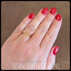 May include: A gold-colored ring with an elongated oval design is displayed on a hand with red nail polish. The ring has a simple, elegant style. The text "SUSANSJEWELRYDESIGNS" is visible at the bottom of the image.