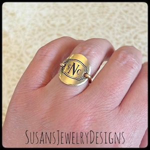 May include: A gold ring with a round, hammered metal top featuring a black engraved monogram "SNC".