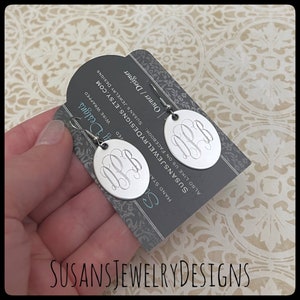 May include: Silver monogram earrings with a round shape. The earrings are on a card with the text "SUSANSJEWELRYDESIGNS.ETSY.COM" and "HAND STAMPED".