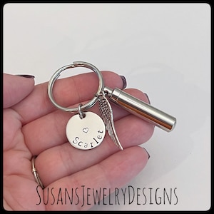 May include: Silver keychain with a small round charm engraved with "Scarlet" and a heart. The keychain also has a small silver angel wing charm and a silver cylinder charm.