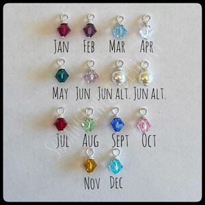 May include: A set of 12 small charms, each representing a different month of the year. The charms are made of silver wire and feature various colored crystals and pearls. The charms are labeled with the month abbreviations: JAN, FEB, MAR, APR, MAY, JUN, JUN ALT, JUN ALT, JUL, AUG, SEPT, OCT, NOV, DEC.