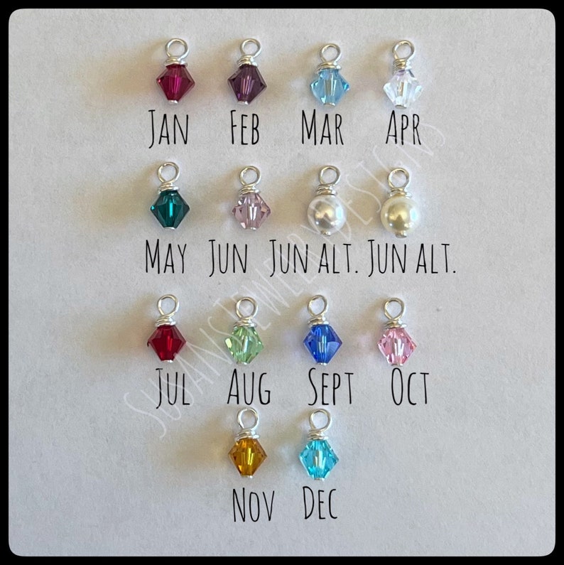May include: A set of 12 small charms, each representing a different month of the year. The charms are made of silver wire and feature various colored crystals and pearls. The charms are labeled with the month abbreviations: JAN, FEB, MAR, APR, MAY, JUN, JUN ALT, JUN ALT, JUL, AUG, SEPT, OCT, NOV, DEC.