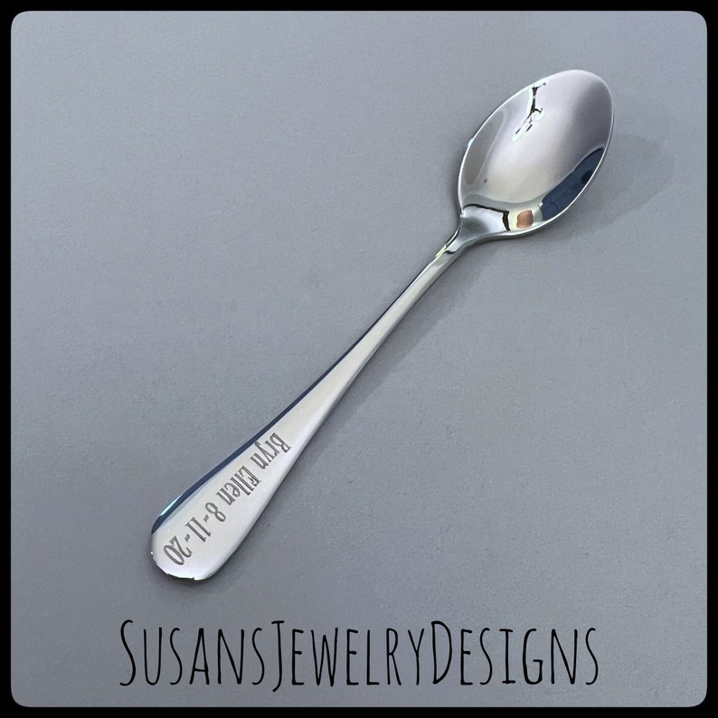 Puede incluir: Una cuchara plateada brillante con un mango largo. La cuchara tiene el texto grabado "Bryn Ellen 8-11-20" en el mango. El texto "SUSANSJEWELRYDESIGNS" est&aacute; en la parte inferior de la imagen.