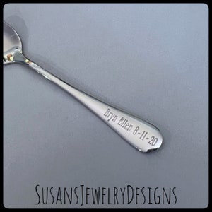 Puede incluir: Una cuchara plateada brillante con la inscripci&oacute;n grabada "Bryn Ellen 8-11-20" en el mango. La cuchara se encuentra sobre un fondo gris. El texto "SUSANSJEWELRYDESIGNS" es visible en la parte inferior.