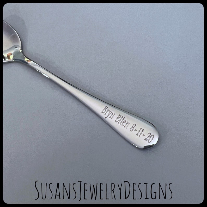 Puede incluir: Una cuchara plateada brillante con la inscripci&oacute;n grabada "Bryn Ellen 8-11-20" en el mango. La cuchara se encuentra sobre un fondo gris. El texto "SUSANSJEWELRYDESIGNS" es visible en la parte inferior.