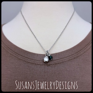 May include: A silver chain necklace with a small silver pendant shaped like an egg and a dark green crystal charm.