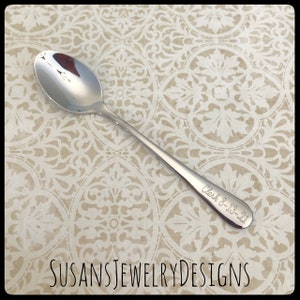 May include: A silver teaspoon with the inscription "Clark 8-18-21" engraved on the handle.  The spoon is on a patterned background.