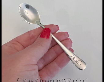 May include: A silver teaspoon with the name "Parker" engraved on the handle. The spoon is being held in a hand.