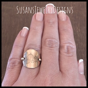 May include: A silver ring with a round, engraved design of three pumpkins. The ring is on a person's finger.