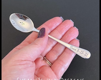 May include: A silver teaspoon with a small engraved design on the bowl and the text "Grace 8-13-21" engraved on the handle.