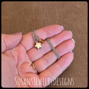May include: A silver chain necklace with a small silver star charm and a small amber-colored crystal charm.
