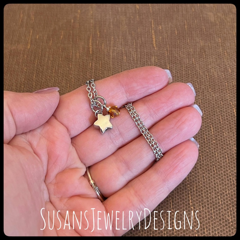 May include: A silver chain necklace with a small silver star charm and a small amber-colored crystal charm.