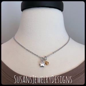 May include: A silver chain necklace with a silver star charm and a small amber-colored gemstone charm.