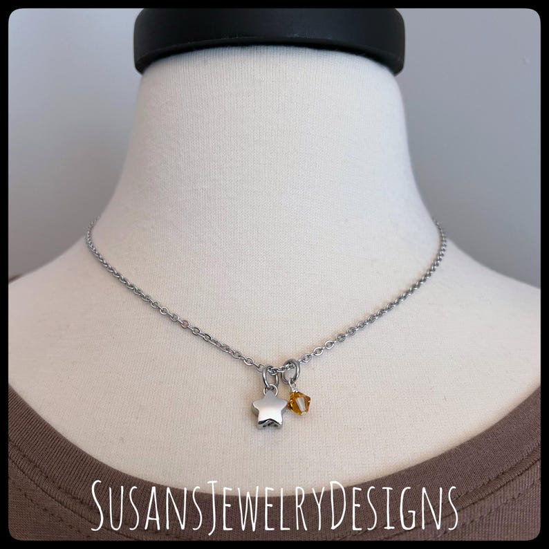 May include: A silver chain necklace with a silver star charm and a small amber-colored gemstone charm.