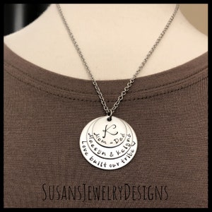 May include: Silver necklace with a layered pendant that reads "Mom & Dad", "Maesyn & Kellynn", and "Love built our tribe".