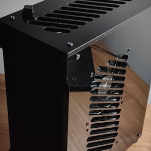 May include: A black computer case with a mesh panel on the side. The case has a power button on the front and a fan visible through the mesh panel.