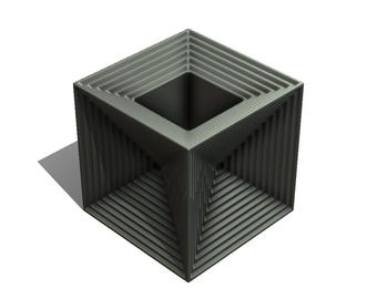 Puede incluir: Una jardinera decorativa gris en forma de cubo con una abertura cuadrada en la parte superior. Los lados presentan una serie de líneas horizontales, creando un efecto de capas. La jardinera proyecta una sombra sobre la superficie blanca.