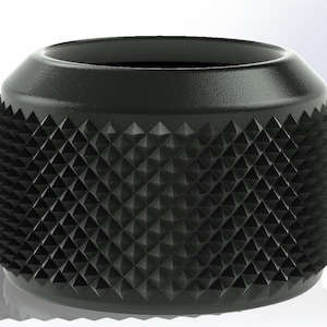 Puede incluir: Un objeto cilíndrico negro con una superficie texturizada con un patrón de diamantes. La parte superior es un borde liso y ligeramente inclinado. Probablemente sea un componente o accesorio, posiblemente para maquinaria o equipos.