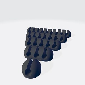 Puede incluir: Un grupo de organizadores de cables negros dispuestos en forma de triángulo. Los organizadores están hechos de plástico flexible y tienen un pequeño agujero en el centro para sujetar los cables.