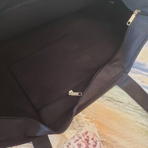 May include: Black canvas tote bag with a zippered pocket and a zipper closure. The bag has two handles.