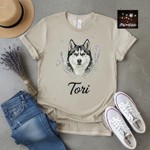 Può includere: T-shirt beige con un'illustrazione di Husky, con pelo bianco e nero, occhi blu e il nome "Tori". Il design include lavanda e farfalle. La maglietta è abbinata a jeans blu e scarpe da ginnastica bianche.