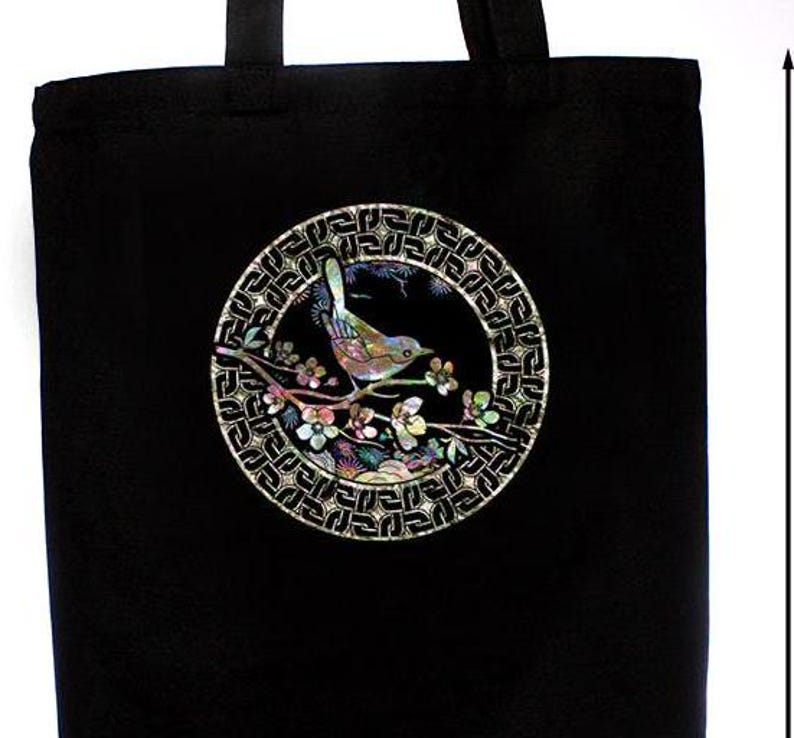 May include: Black tote bag with a circular design featuring a bird perched on a branch with flowers. The design is made of iridescent mother-of-pearl inlay.