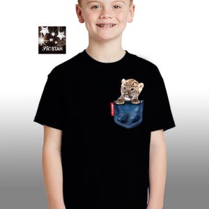 May include: A black t-shirt with a blue pocket featuring a small leopard cub peeking out. The t-shirt has short sleeves and a crew neck.