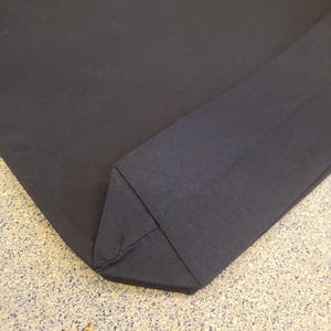May include: A close-up of a black fabric corner, showing the stitching detail. The fabric is folded over itself, creating a sharp, clean edge.