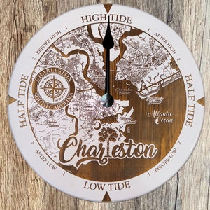 May include: A white and brown wooden clock with a map of Charleston, South Carolina, and the words "Charleston" and "High Tide" and "Low Tide". The clock has a black hand pointing to the time.